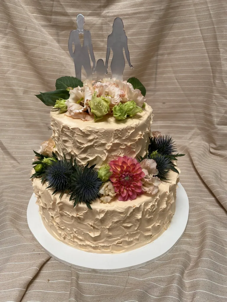 Zweistöckige Hochzeitstorte mit frischen Blüten und Brautpaar-Aufsatz